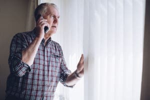 Man holding a cell phone and looking out his window representing the need for an animal abuse attorney